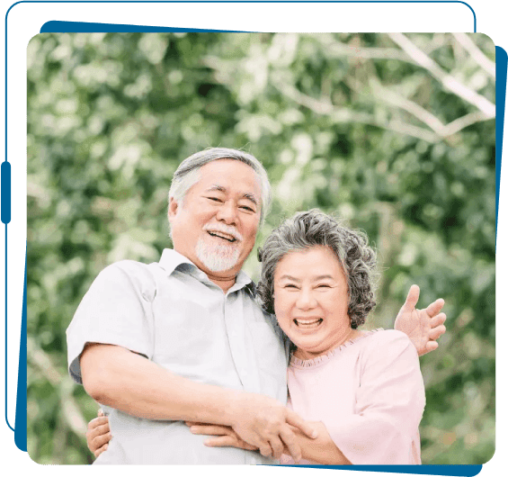 An older couple posing for a picture in front of trees.